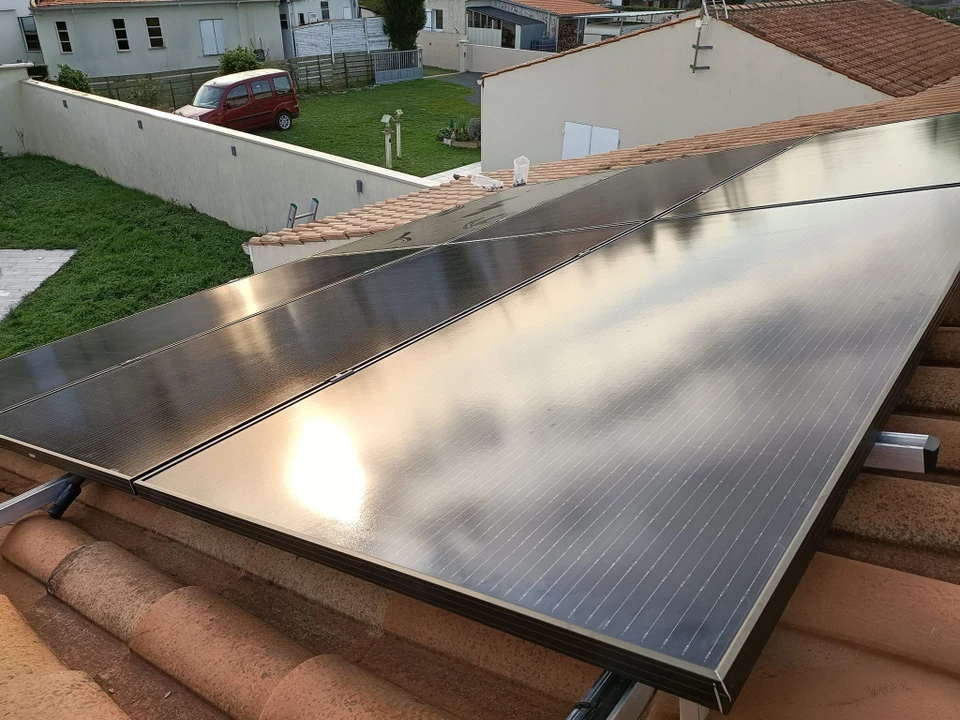 Borne de recharge pour véhicule électrique murale, modèle compact blanc avec voyant lumineux vert, fixée sur un mur de briques bicolore (rouge et blanc) en extérieur