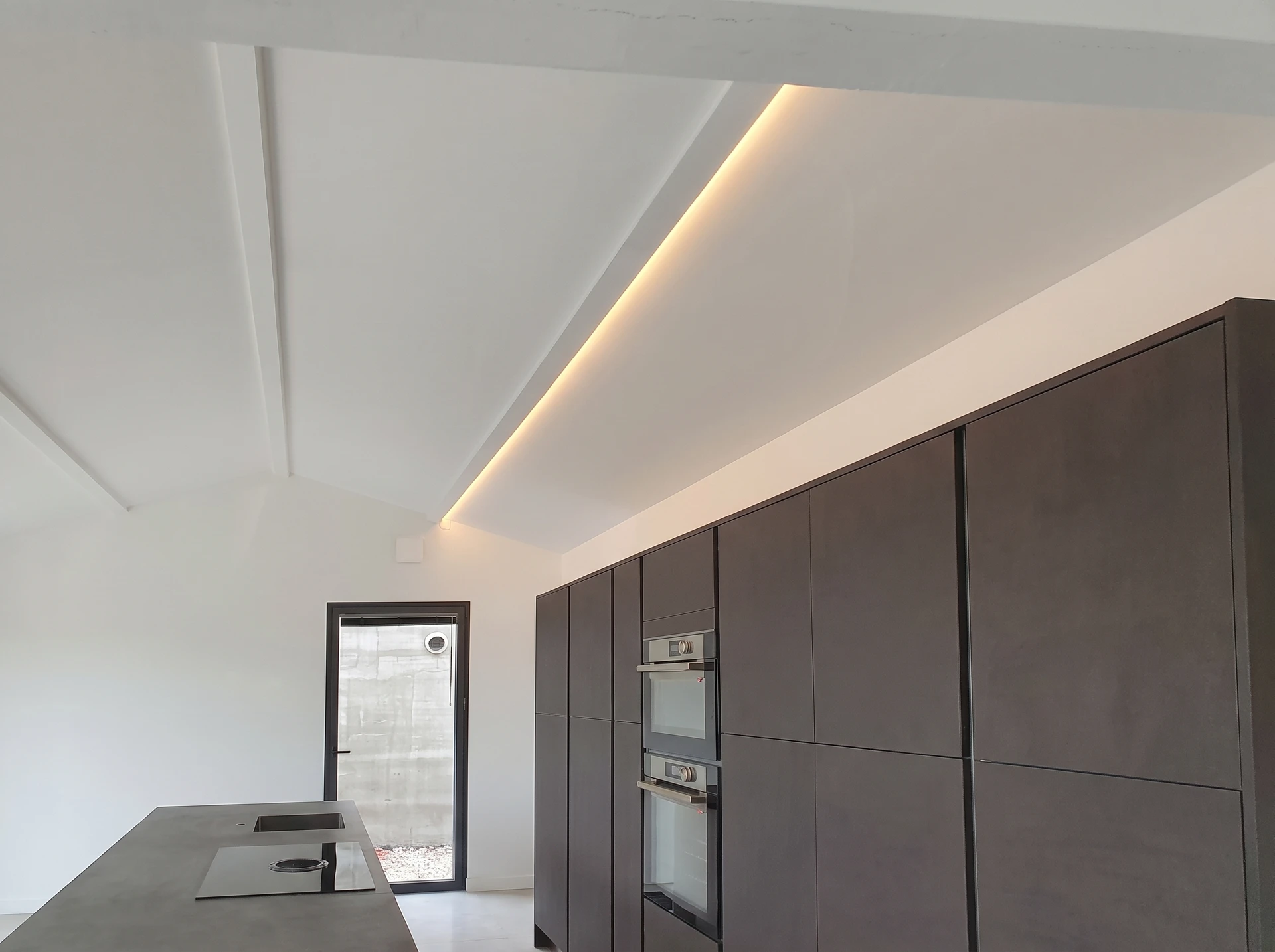 Technicien électricien en tenue professionnelle standard (polo blanc ou gris) tenant un mètre laser ou une règle, prenant les dimensions d'une pièce résidentielle avant installation de climatisation murale. Tableau blanc avec schéma de dimensionnement VMC visibles sur le mur en arrière-plan. Environnement intérieur résidentiel, clair, professionnel.