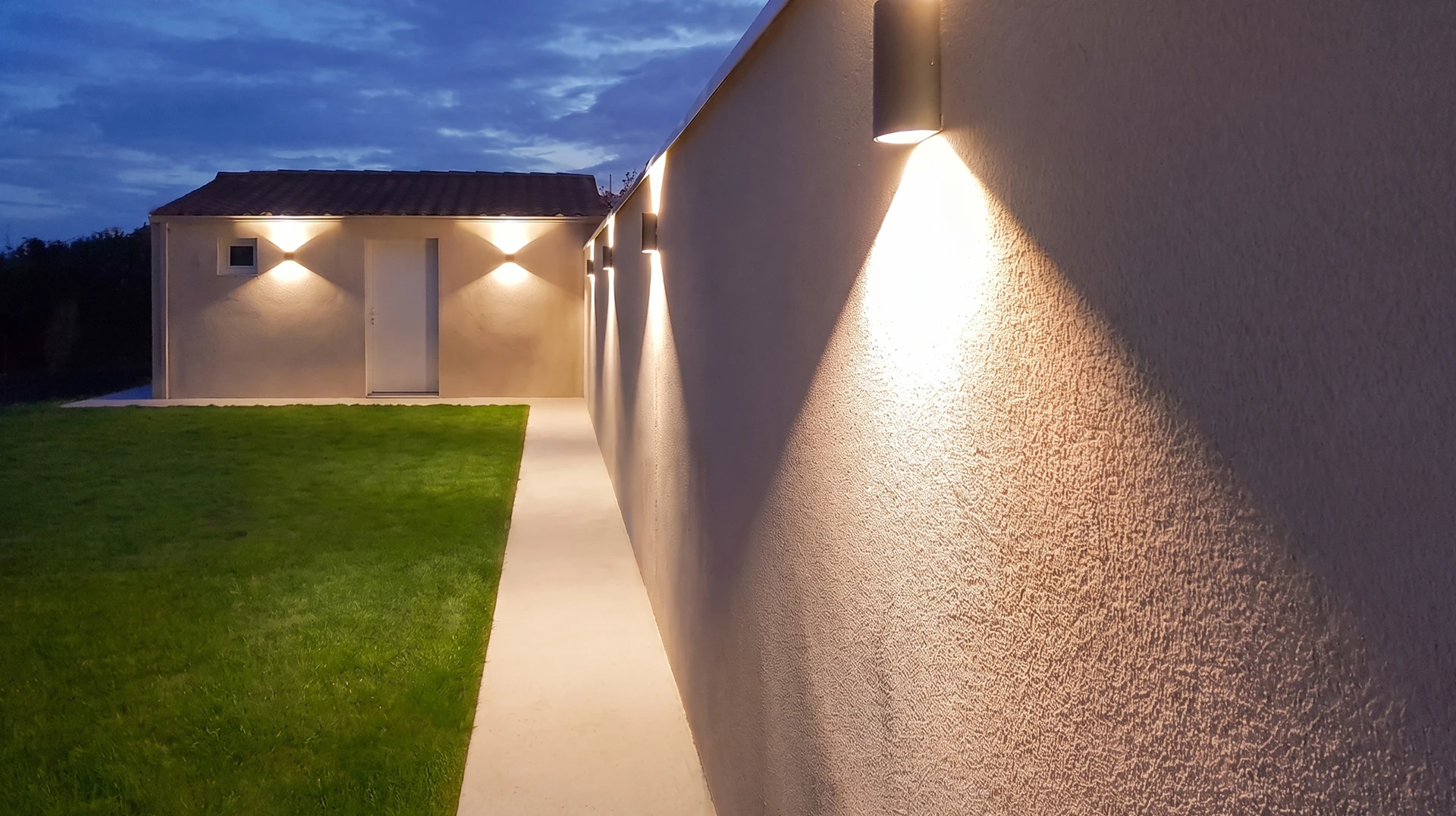 Électricien en tenue de travail professionnelle, equipé d'une ceinture à outils, fixant un tableau électrique modulaire gris avec disjoncteurs sur la paroi d'une maison en rénovation, mur blanc BA13 visible, prise de vue en légère plongée montrant précision et professionnalisme du geste technique.